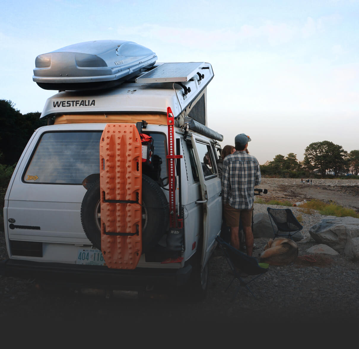 A car with a pop up tent on the roof and various camping equipment. 