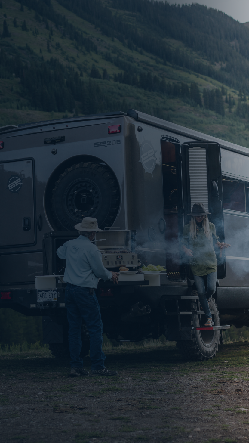 People grilling outside of a camping van parked in the mountains.