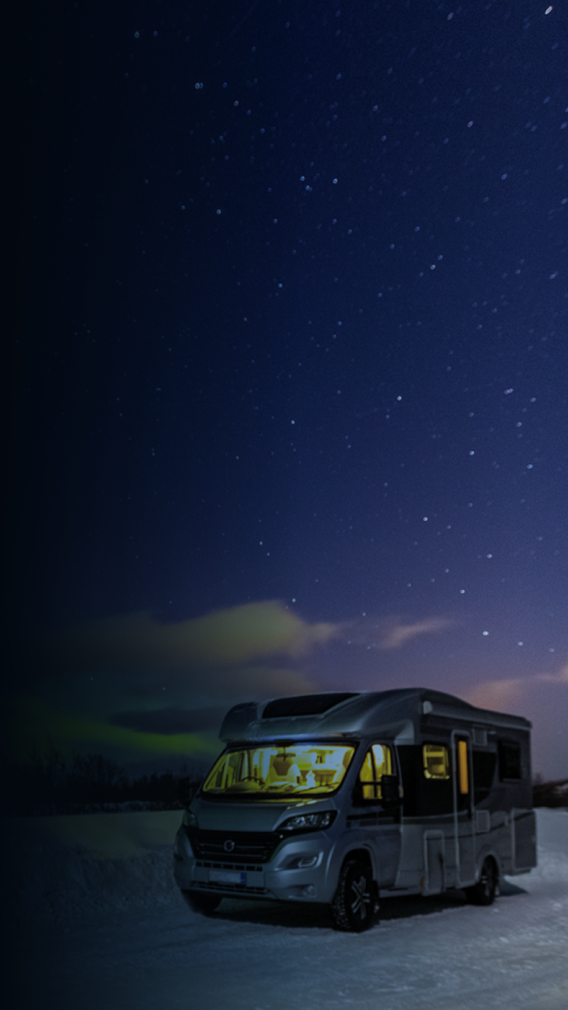 A lit-up RV in a snowy area with the stars and northern lights in the sky. 