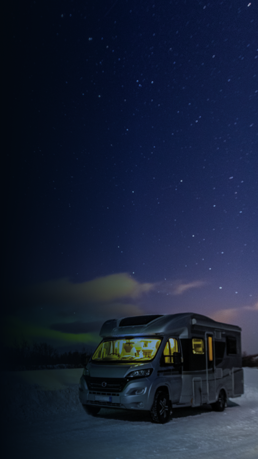 A lit-up RV in a snowy area with the stars and northern lights in the sky.